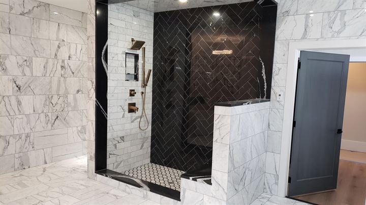 Marble-clad walk-in shower with a black herringbone accent wall and niche