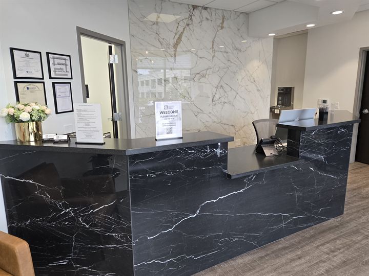 Reception desk wrapped in black marble-look slab in front of a large-format white marble-look feature wall