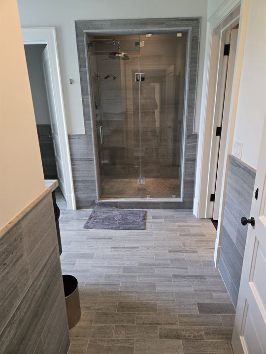 Hallway with wood-look plank tile leading to a glass steam shower clad in gray tile