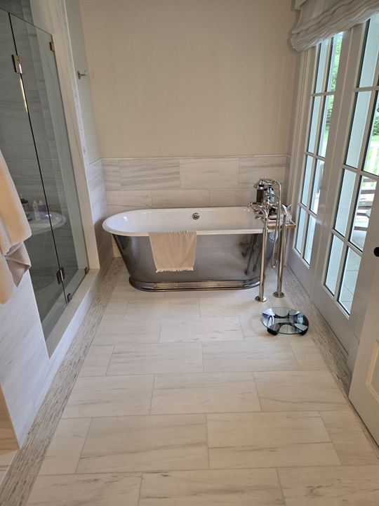 Primary bath with a large-format white marble floor, marble wainscot and a freestanding soaking tub