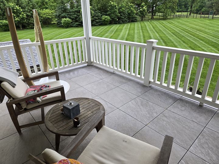Covered porch floored with large gray porcelain pavers overlooking a lawn