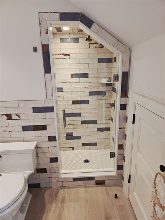 Shower under a sloped ceiling clad in white and blue reclaimed-look subway tile