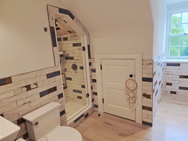 Bathroom with a reclaimed-look subway tile wainscot and an angled shower under the eaves